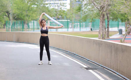 Portrait of sporty young asian woman in sportswear jogging outdoor for marathon training. Jogger girl stretching along concrete path outdoor with green tree background. Sport conceptの写真素材