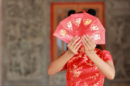 Beautiful Asian woman hands in red Chinese dress traditional cheongsam qipao with gesture of showing red envelope or Any Pao, text means good luck entering the house (Chinese new year)の写真素材