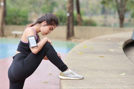 Athletic young healthy and beauty asian woman in sportswear standing and stretching outdoor for morning exercise. Active girl work out on biceps practice with mobile phone. Sport and lifestyle conceptの写真素材