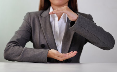 Attractive professional female hands in classic suit show protecting something on table. Businesswoman sitting with white background. Property insurance and security conceptの写真素材