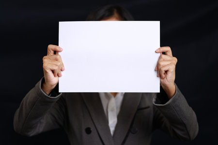 Attractive professional female hands standing and showing blank sheet of paper for advertising on black background isolatedの写真素材