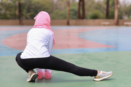 Rear view athletic young beauty asian woman in muslim sportswear stretching and lifting dumbbells public exercise. Active girl work out on biceps exercise with green tree background. Sport conceptの写真素材