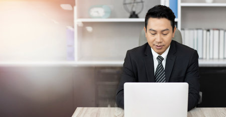 Successful asian businessman working on data analyzing from computer. Middle aged business man talking to colleague team in video call conference and work online, sitting in modern corporate officeの写真素材