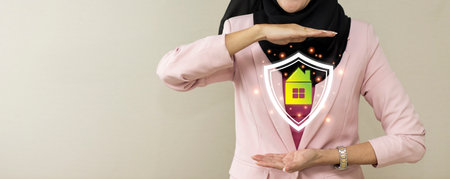 Attractive professional asian muslim female show protecting house futuristic graphic with shield. Businesswoman standing in modern office with white background. Property insurance and security conceptの写真素材