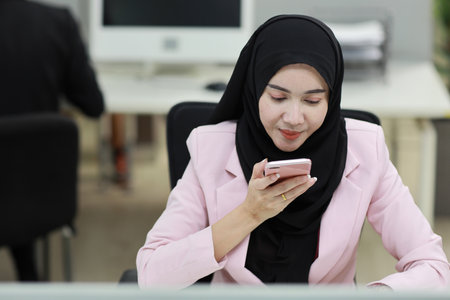 Attractive professional asian muslim female employee worker sitting, using laptop computer with coworker at workplace. Businesswoman talking on smart mobile phone and communicate with client.の写真素材