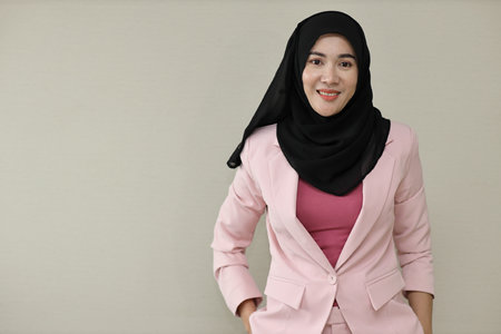 Happy and smart asian business woman in muslim dress standing and holding hands pockets with confident. Isolated background portrait with smiling beauty face in hijab. Advertisement portrait conceptの写真素材