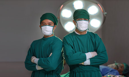 Professional surgical team arms crossed with patient blurred background on hospital bed in hospital operating room. Medical technology, treatment, healthcare, surgery and health insurance conceptの写真素材