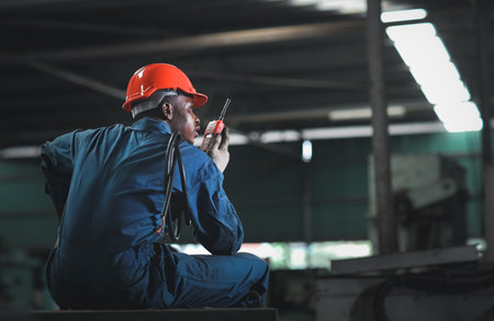 Rear view of engineer or worker man in protective uniform sitting and using walkie talkie radio...