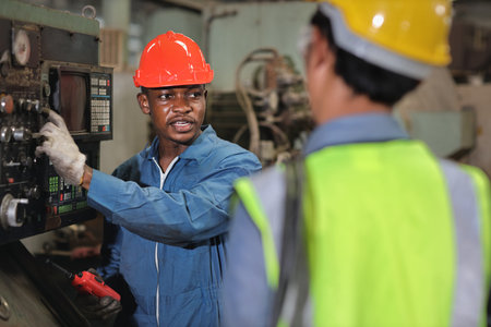 Technician engineer in protective uniform with hardhat standing and teaching apprentices or...