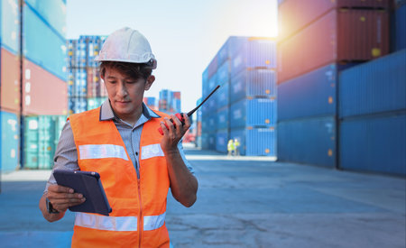 Foreman using walkie talkie radio and tablet control loading containers box. Engineer or worker with...