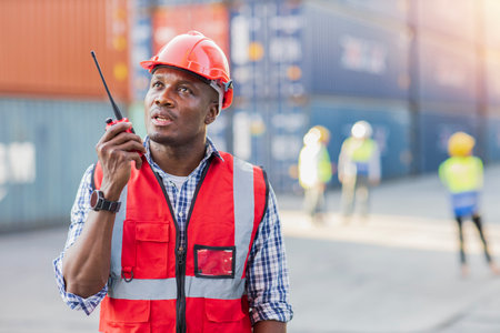 Foreman engineer using walkie talkie radio control loading containers box. Confident engineering with helmet work at container cargo site and checking industrial container cargo freight shipの写真素材