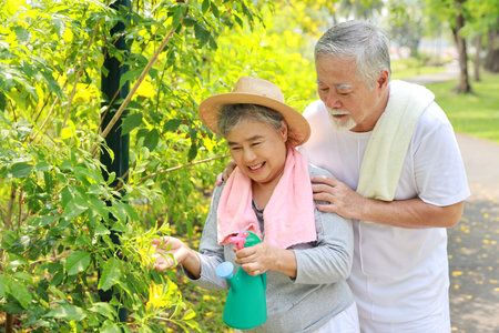 Asian senior couple incasual embracing and spending time in garden backyard while watering flowers plants with laughing and smiling on sunny day after retired. Happy elderly outdoor lifestyle concept.の写真素材