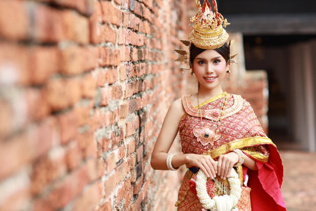 Happ smiling young fashion and beautiful asian woman in Thai red traditional costume with jasmine flower garland standing outdoor in ancient buddha temple Ayutthaya, Thailand. Travel conceptの写真素材