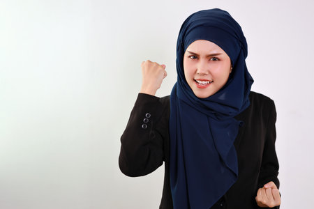 Happy smart asian business woman in muslim dress standing, raising hands and looking at camera with confident in studio. Isolated white background portrait with beautiful face in hijab.の写真素材