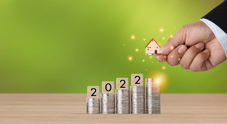 Business property investment with business man hand stacking coin growing growth with house model and year number 2022 on wooden desk and green background for financial real estate advertising conceptの写真素材
