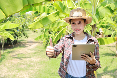 Asian agronomist or woman farmer show thumb up and reading report growing crops data from tablet for increasing productivity in agriculture field, modern smart farming with technology conceptの写真素材