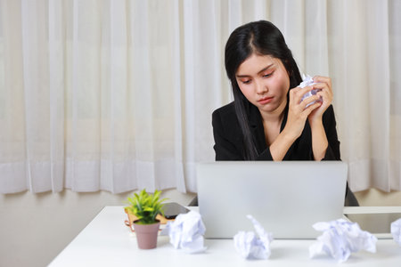 Mid adult businesswoman feeling upset  after bad news business failure or get fired and feeling discouraged, distraught and hopeless on blue background with computer and crumpled paperの写真素材