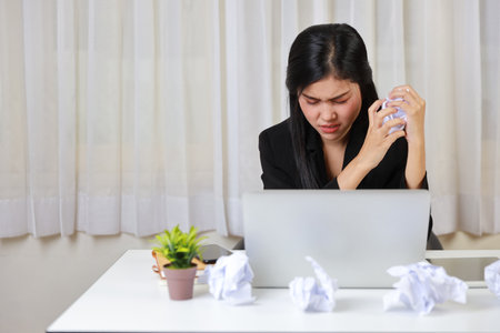 Mid adult businesswoman feeling upset  after bad news business failure or get fired and feeling discouraged, distraught and hopeless on blue background with computer and crumpled paperの写真素材