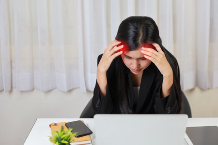 Young asian stressed businesswoman having problem or feeling pain touch temples suffer headache or migraine after working on computer for too long time. Office syndrome conceptの写真素材
