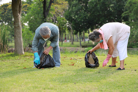volunteer tourist asian senior couple cleaning up garbage and plastic debris on dirty park by collecting them into big black bagの写真素材