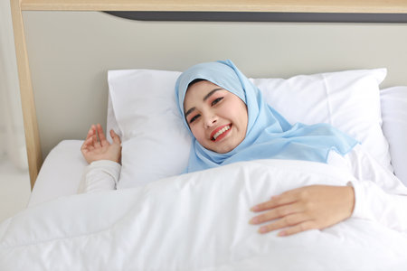 Oversleeping asian woman wearing white muslim sleepwear lying on bed with happiness.Top view portrait young cute girl sleeping in bedroom with happy and beauty face. Lifestyle conceptの写真素材
