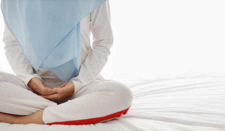 Close up young asian woman hand sitting on bed and enjoying meditation. Beautiful girl in muslim sleepwear with blue hijab practices yoga in bedroom with peace and calm. Healthy and lifestyle conceptの写真素材