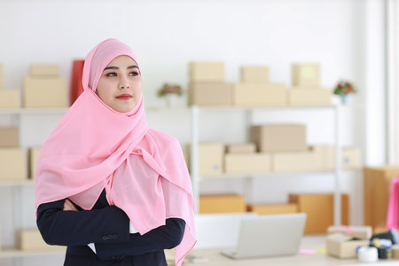 Religious asian woman in blue muslim suit and pink shaft on head standing and looking at camera with confidence. Business woman stand with package SME box delivery background. Work at home conceptの写真素材