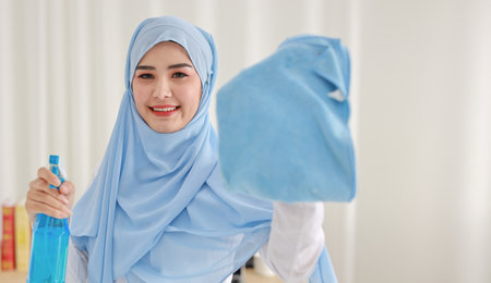 Indoor shot active young beautiful asian housewife woman holding cleaning spray, washing table. Portrait cute girl with happy emotional cleaning bedroom in new apartment after moved in.の写真素材