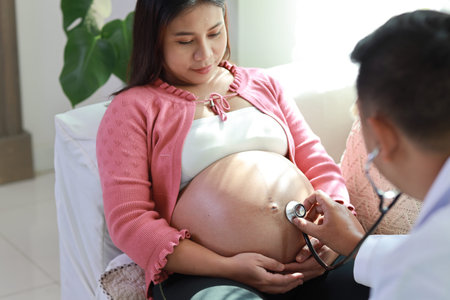 Happy young asian pregnant female and male doctor standing on sofa in living room at home with...