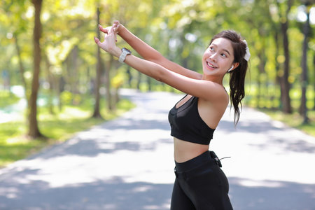 Portrait of happy young asian sportswoman practice yoga stretching and meditation exercise after finish morning run outdoor. Beautiful athlete smile woman listening music under the tree in the parkの写真素材