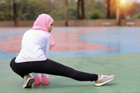 Rear view athletic young beauty asian woman in muslim sportswear stretching and lifting dumbbells public exercise. Active girl work out on biceps exercise with green tree background. Sport conceptの写真素材