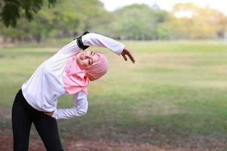 Public exercise lifestyle concept, fitness woman listening music from wireless earphones and mobile phone. Rear view athletic young asian girl in muslim sportswear standing, stretching after workoutの写真素材