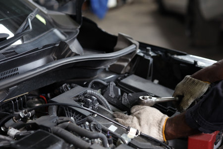 Man technician car mechanic hamds in half uniform checking maintenance a car service at repair garage station. Worker holding wrench and fixing breakdown vehicle. Concept of car center repair service.の写真素材
