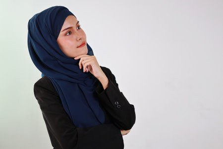 Smart asian business woman in muslim dress standing and holding chin while crossed arms and looking away with confident in studio. Isolated white background portrait with beautiful face in hijab.の写真素材
