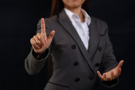 Attractive professional female hands in classic suit pointing while show holding something. Businesswoman standing with black background. Property insurance and security conceptの写真素材