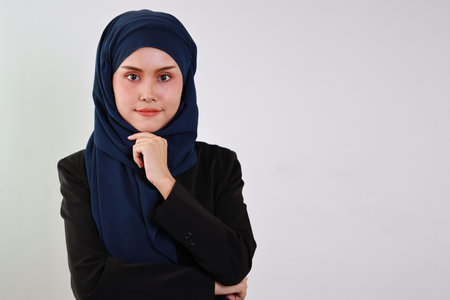 Smart asian business woman in muslim dress standing and holding chin while crossed arms and looking at camera with confident in studio. Isolated white background portrait with beautiful face in hijab.の写真素材