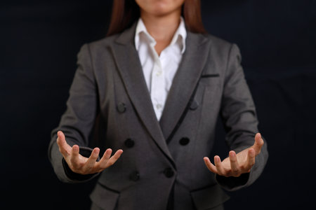 Attractive professional female hands in classic suit show protecting something. Businesswoman standing with black background. Property insurance and security conceptの写真素材