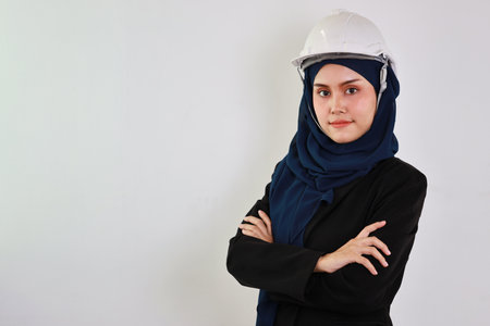 Happy and smart muslim asian engineer standing and arms cross with confident in studio. Isolated white background image with beautiful face female and hard hat in hijab. Advertisement portrait conceptの写真素材