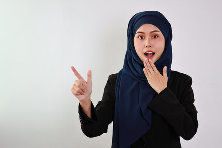 Happy smart asian business woman in muslim dress standing and pointing something with confident in studio. Isolated white background portrait beautiful face in hijab. Advertisement portrait conceptの写真素材
