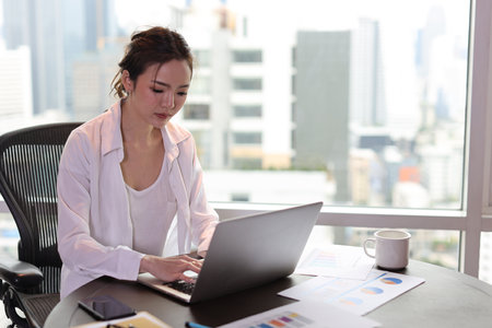 Portrait of confident and beautiful young asian businesswoman with happy emotion sitting and using computer in modern hotel with city blurred background. Success business and lifestyle conceptの写真素材