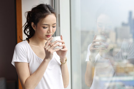 Portrait of confident and beauty young asian businesswoman with coffee cup standing and looking away in modern hotel with city blurred background. Success business and lifestyle conceptの写真素材