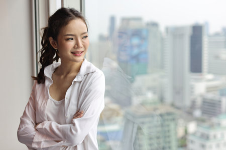Portrait of confident and beautiful young asian businesswoman with happy smiling face standing and looking away in modern hotel with city blurred background. Success business and lifestyle conceptの写真素材
