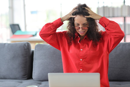 Mid adult businesswoman touching her head on sofa in living room after bad news business failure or get fired and feeling discouraged, distraught and hopeless in apartment or home office.の写真素材
