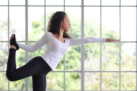 Sporty young adult woman stand on yoga mat practicing mediate yoga watching coach training video online from laptop. Healthy female doing exercise and taking lesson distant course among nature outdoorの写真素材
