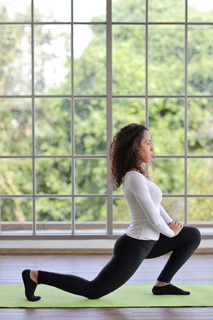 Sporty young adult woman sit on yoga mat practicing mediate yoga watching coach training video online from laptop. Healthy female doing exercise and taking lesson distant course among nature outdoorの写真素材