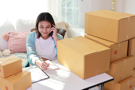 Attractive happy asian pregnant woman sitting and using mobile smart phone and writing order for customer with tablet. Expectant mother preparing and working for baby birth during pregnancy concept.の写真素材