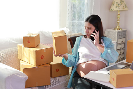 Attractive happy asian pregnant woman sitting and using mobile smart phone and checking order for customer with tablet. Expectant mother preparing and working for baby birth during pregnancy concept.の写真素材