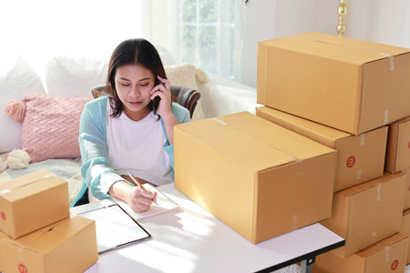 Attractive happy asian pregnant woman sitting and using mobile smart phone and writing order for customer with tablet. Expectant mother preparing and working for baby birth during pregnancy concept.の写真素材