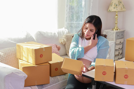 Attractive happy asian pregnant woman sitting and using mobile smart phone and checking order for customer with tablet. Expectant mother preparing and working for baby birth during pregnancy concept.の写真素材