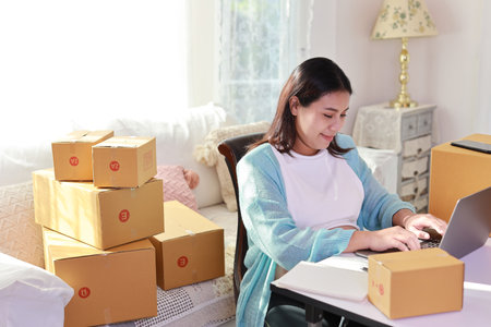 Attractive happy asian pregnant woman sitting and using mobile smart phone and making order for customer with computer. Expectant mother preparing and working for baby birth during pregnancy conceptの写真素材